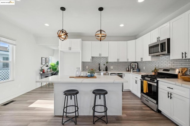 kitchen featuring decorative light fixtures, a center island, white cabinets, and appliances with stainless steel finishes