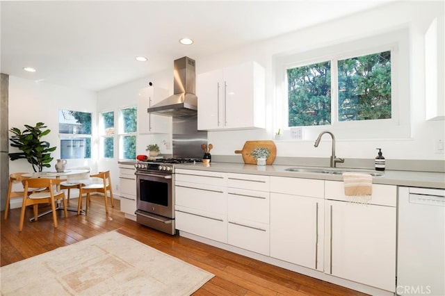 kitchen featuring wall chimney exhaust hood, sink, stainless steel range with gas cooktop, dishwasher, and white cabinets