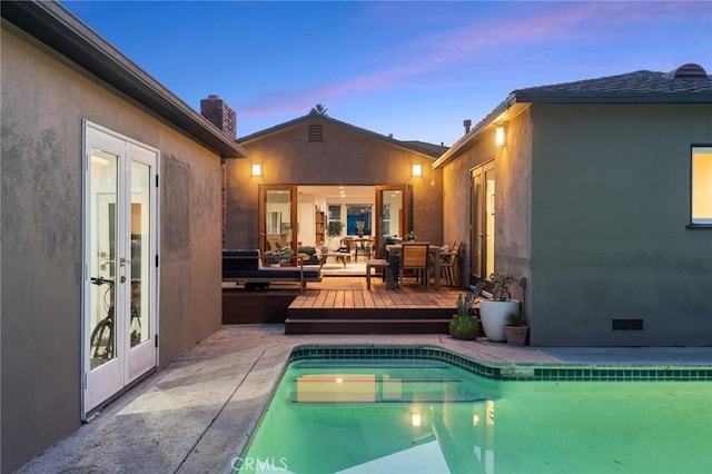 pool at dusk with a wooden deck and french doors