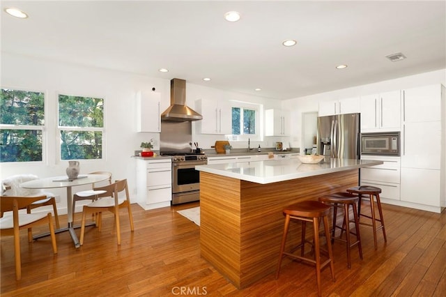 kitchen with white cabinetry, stainless steel appliances, a kitchen island, and wall chimney range hood