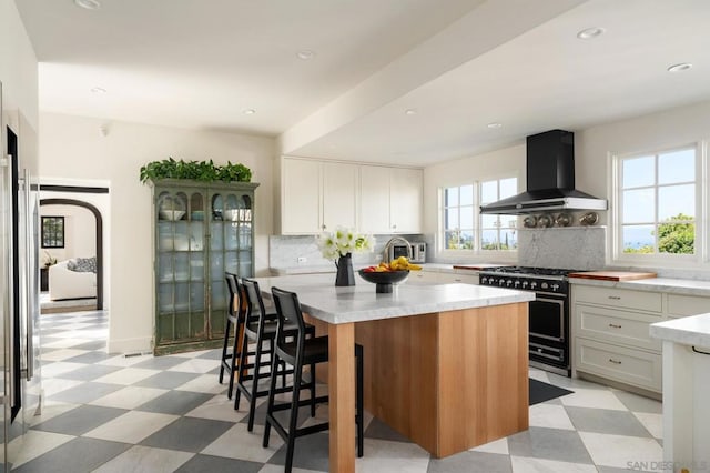 kitchen featuring white cabinets, range with gas stovetop, a center island with sink, and wall chimney exhaust hood