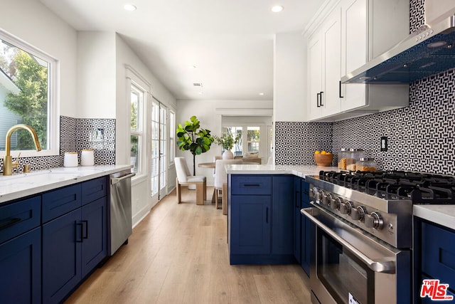 kitchen featuring white cabinetry, sink, blue cabinets, stainless steel appliances, and wall chimney exhaust hood