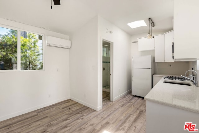 kitchen featuring an AC wall unit, white fridge, white cabinets, light wood-type flooring, and sink