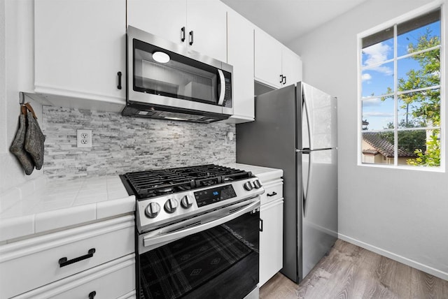 kitchen featuring stainless steel appliances, tile counters, white cabinets, and decorative backsplash