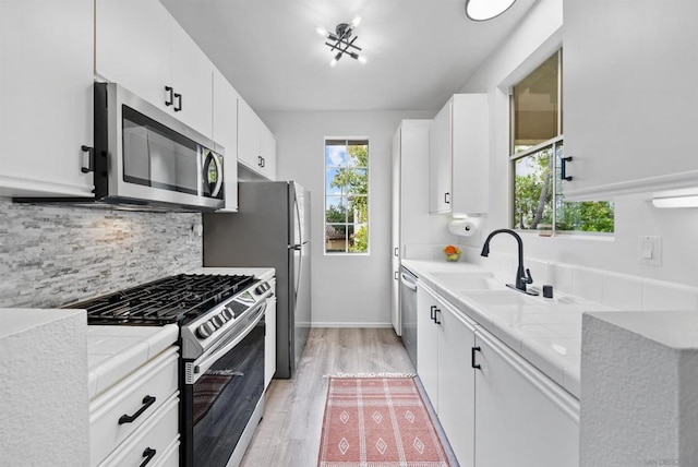 kitchen with appliances with stainless steel finishes, sink, white cabinets, light hardwood / wood-style floors, and plenty of natural light