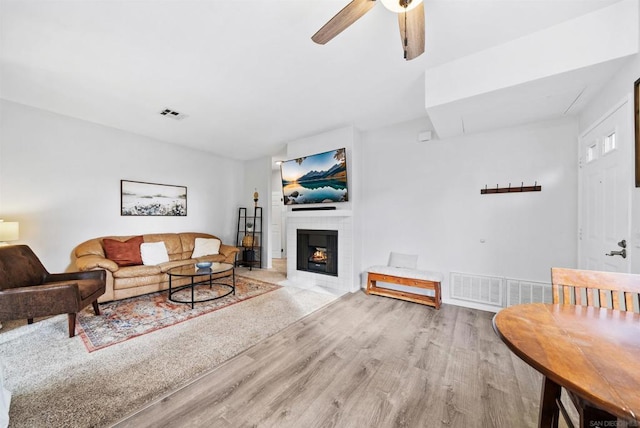 living room with a tiled fireplace, light hardwood / wood-style floors, and ceiling fan