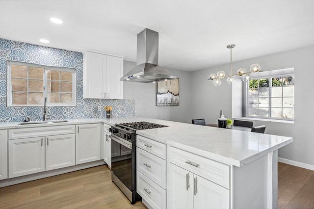 kitchen featuring gas range, sink, decorative light fixtures, white cabinets, and island exhaust hood