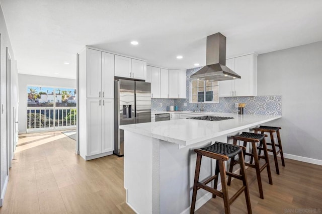 kitchen with appliances with stainless steel finishes, island range hood, white cabinets, kitchen peninsula, and a breakfast bar