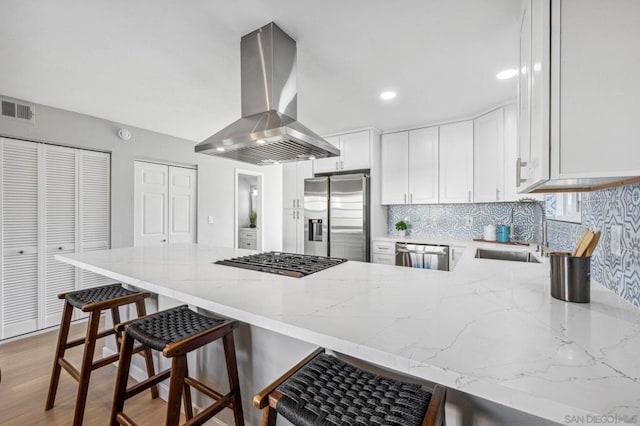 kitchen featuring white cabinets, island exhaust hood, stainless steel appliances, kitchen peninsula, and a breakfast bar area