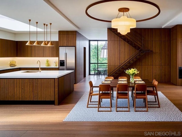 kitchen with high quality fridge, pendant lighting, wood walls, sink, and light hardwood / wood-style floors