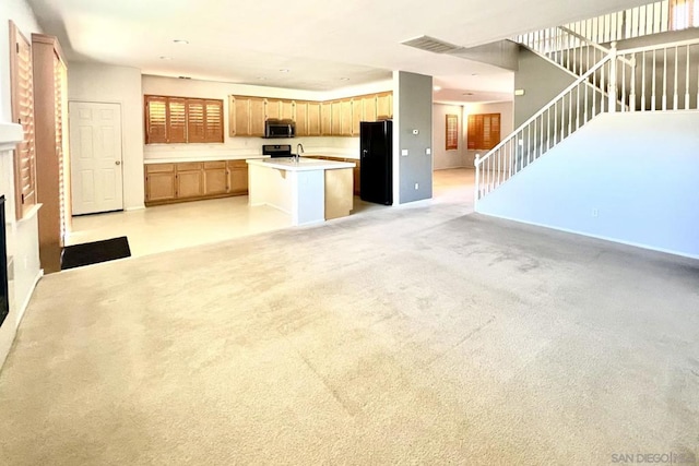 kitchen with light brown cabinetry, range, light carpet, black refrigerator, and a kitchen island with sink