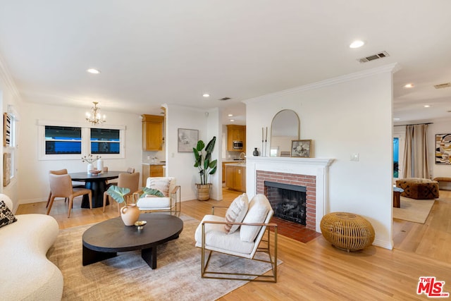 living room featuring a notable chandelier, a brick fireplace, light hardwood / wood-style flooring, and crown molding