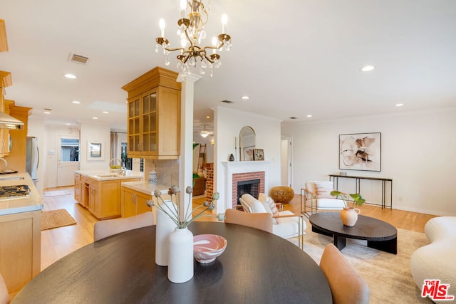 dining room featuring a fireplace, sink, ornamental molding, light hardwood / wood-style flooring, and ceiling fan