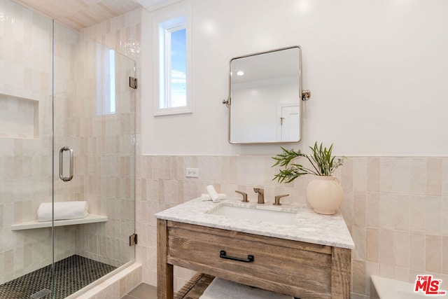 bathroom with a shower with shower door, tile walls, and vanity