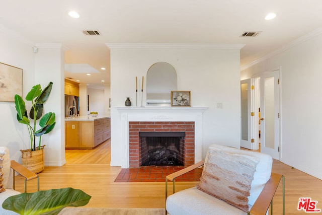 living room featuring crown molding, sink, light hardwood / wood-style flooring, and a brick fireplace