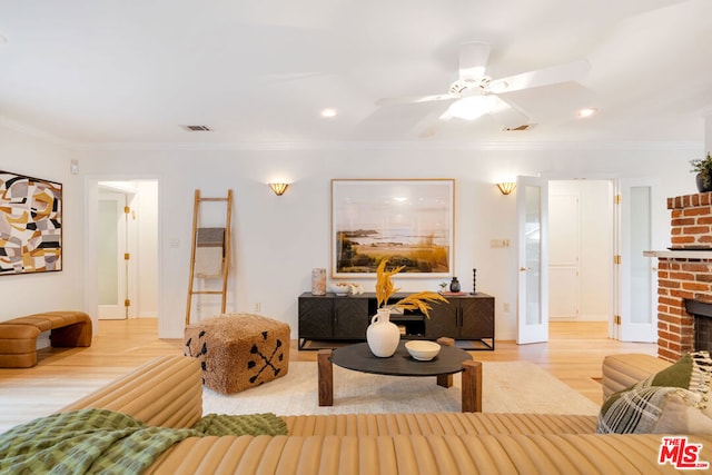 living room featuring crown molding, hardwood / wood-style flooring, ceiling fan, and a brick fireplace