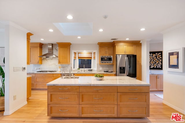 kitchen with a skylight, sink, light hardwood / wood-style flooring, stainless steel appliances, and wall chimney exhaust hood