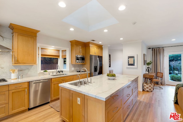 kitchen with backsplash, appliances with stainless steel finishes, light hardwood / wood-style flooring, and a kitchen island with sink