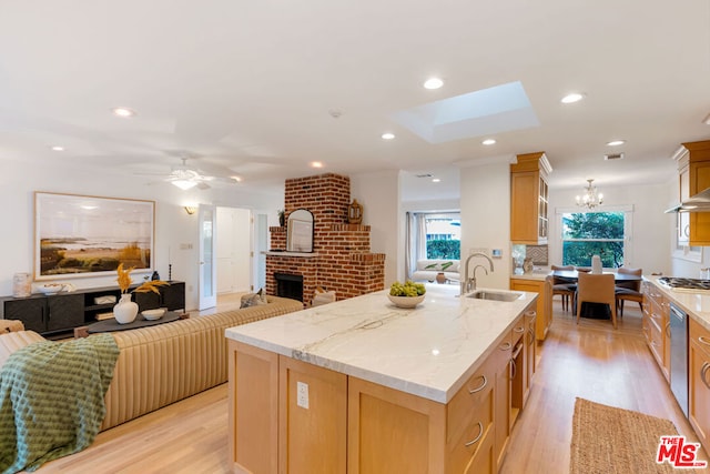 kitchen with light stone countertops, a fireplace, an island with sink, sink, and stainless steel gas cooktop