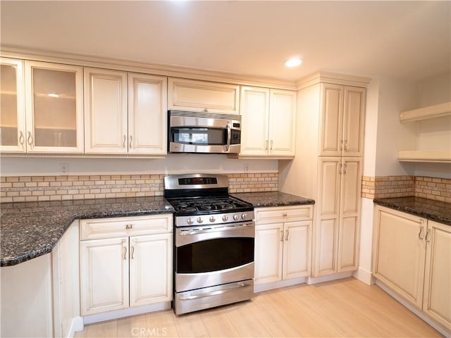 kitchen with stainless steel appliances, light hardwood / wood-style flooring, backsplash, and dark stone counters