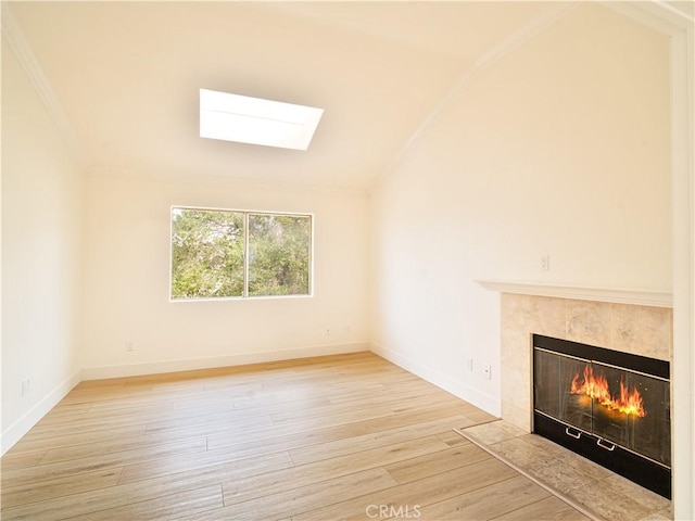 unfurnished living room with a tiled fireplace, lofted ceiling with skylight, and light hardwood / wood-style flooring