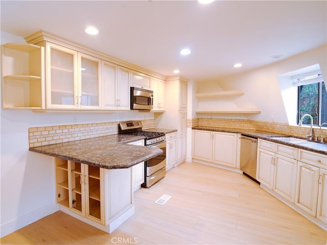 kitchen with sink, light wood-type flooring, dark stone counters, kitchen peninsula, and stainless steel appliances