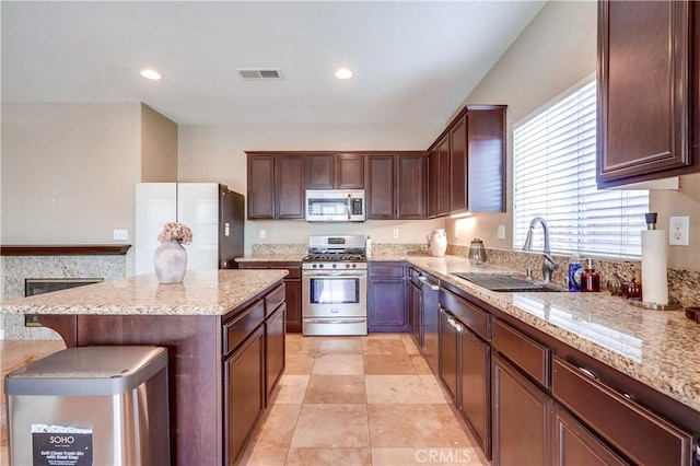 kitchen featuring appliances with stainless steel finishes, sink, light tile patterned floors, light stone countertops, and a kitchen bar