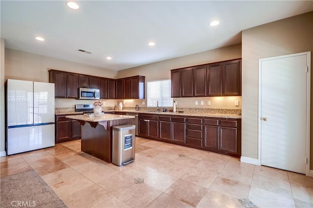 kitchen with dark brown cabinets, light stone counters, a center island, a breakfast bar area, and stainless steel appliances