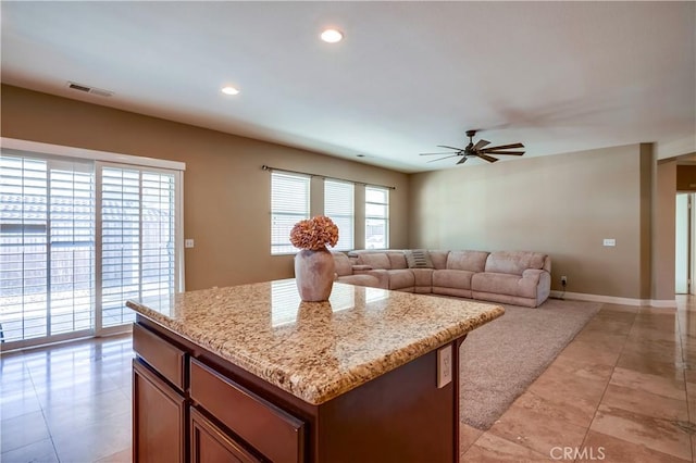 kitchen featuring ceiling fan, a center island, and light stone countertops