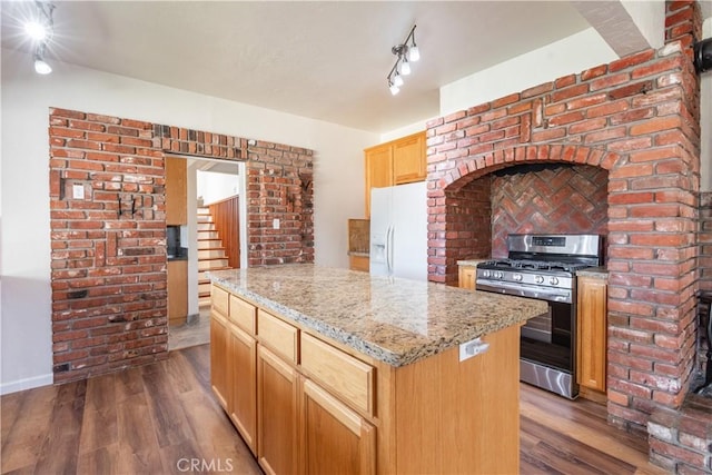 kitchen featuring white fridge with ice dispenser, gas range, a kitchen island, light stone counters, and dark hardwood / wood-style floors