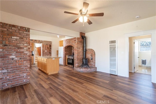 unfurnished living room with a wood stove, brick wall, and dark hardwood / wood-style flooring