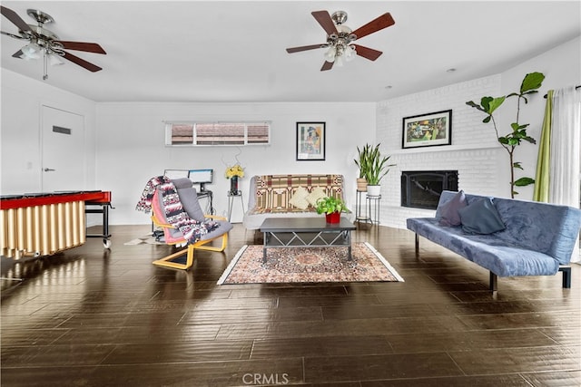 living room featuring a brick fireplace, dark wood-type flooring, and ceiling fan