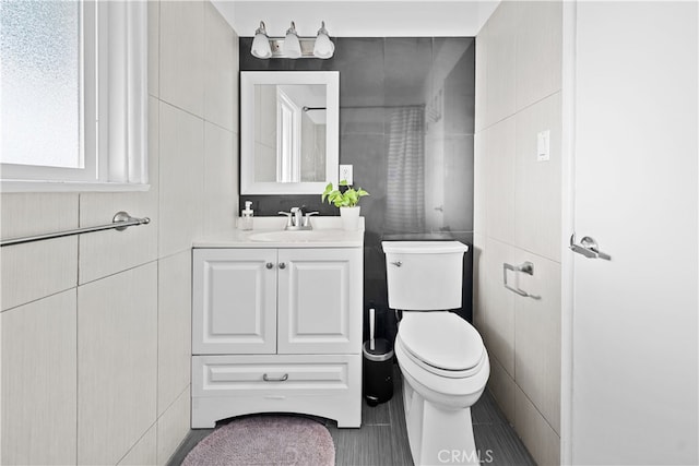 bathroom with tile patterned flooring, vanity, tile walls, and toilet