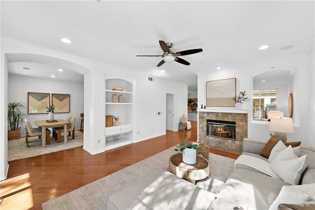 living room featuring dark hardwood / wood-style flooring, a fireplace, built in features, ornamental molding, and ceiling fan