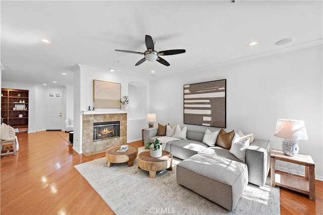 living room featuring crown molding, light hardwood / wood-style flooring, ceiling fan, built in features, and a fireplace