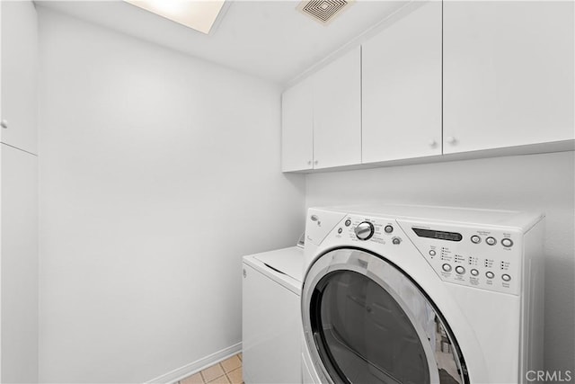 clothes washing area with cabinets, washing machine and dryer, and light tile patterned floors