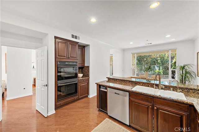 kitchen featuring black double oven, stainless steel dishwasher, sink, backsplash, and light stone counters