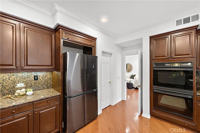 kitchen with black double oven, decorative backsplash, ornamental molding, light stone counters, and stainless steel fridge