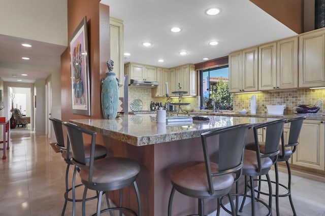 kitchen featuring a kitchen breakfast bar, backsplash, cream cabinets, and dark stone countertops