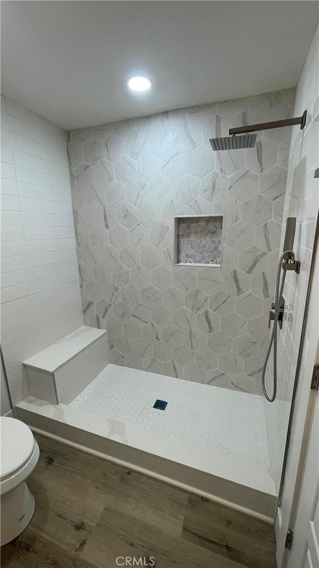 bathroom featuring a tile shower, wood-type flooring, and toilet