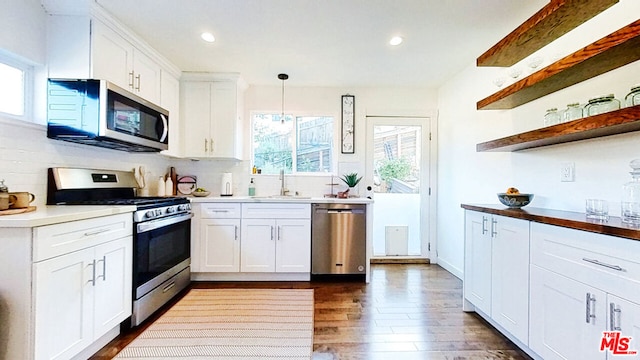 kitchen featuring appliances with stainless steel finishes, decorative light fixtures, sink, white cabinets, and dark wood-type flooring