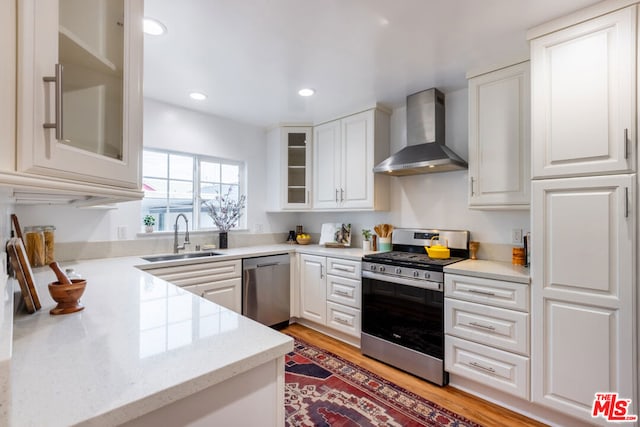 kitchen featuring appliances with stainless steel finishes, wall chimney exhaust hood, white cabinetry, sink, and light wood-type flooring