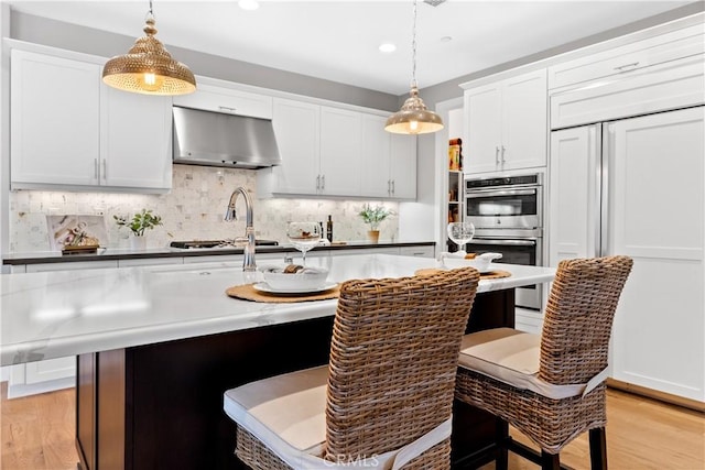 kitchen featuring stainless steel appliances, ventilation hood, hanging light fixtures, and white cabinets