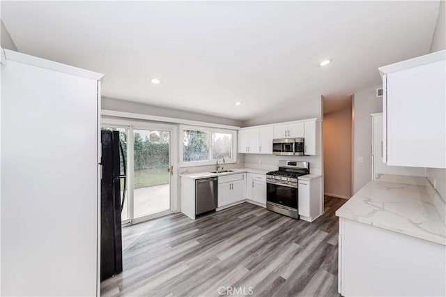 kitchen with white cabinetry, light hardwood / wood-style flooring, stainless steel appliances, light stone counters, and lofted ceiling