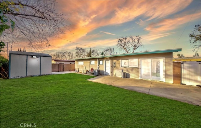 back of property with an outbuilding, a storage unit, a lawn, fence, and cooling unit