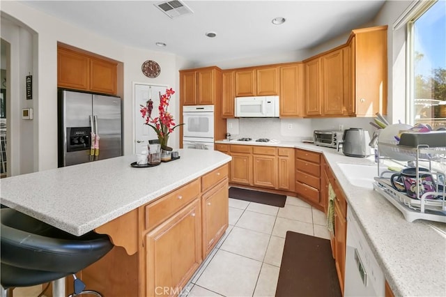 kitchen with sink, backsplash, a kitchen breakfast bar, light tile patterned floors, and white appliances