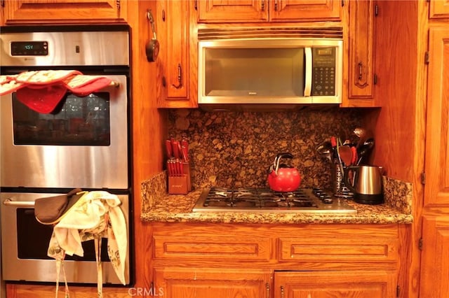 kitchen with light stone countertops, appliances with stainless steel finishes, and tasteful backsplash