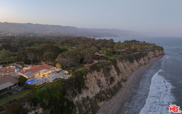 aerial view at dusk featuring a water view and a beach view