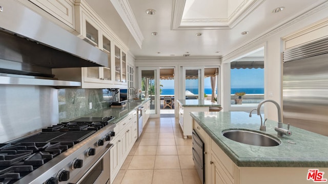 kitchen featuring light tile patterned floors, sink, a water view, backsplash, and an island with sink