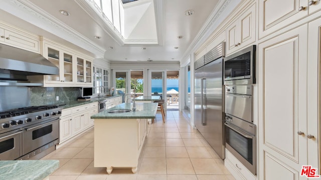 kitchen featuring exhaust hood, a center island with sink, built in appliances, and light tile patterned flooring